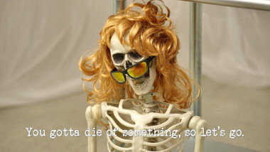 Image of a replica human skeleton wearing a long, tousled blonde wig and a pair of sunglasses (a reference to Lisa McCune's attempt at the 'Unveil something unsophisticated with a smoke machine' task), with the episode title 'You gotta die of something, so let’s go' superimposed on it.