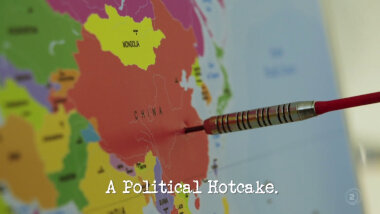 Image of a map of the world, with a dart sticking out of China (a reference to the 'Write and perform a national anthem' task), with the episode title, 'A political hotcake', superimposed on it.