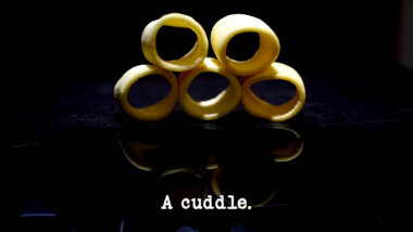 Image of five Hula Hoops potato crisps stacked up in a pyramid (a reference to the 'Find and put the gold rings on the stick' task), with the episode title, 'A cuddle', superimposed on it.