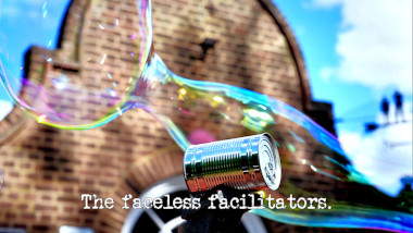 Photo of a tin can laid on its side, with a large soap bubble behind it, in front of the Taskmaster house (referencing the 'Knock over exactly 100 cans' and 'Do the most beautiful thing with bubbles' tasks), with the episode title, 'The faceless facilitators', superimposed on it.