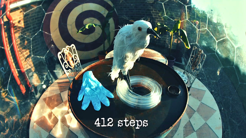 Photo of a fake taxidermy egret on top of an oil drum, alongside a surgical glove and a coil of plastic tubing (referencing the 'Do something you regret', 'Put all the gloves back in the glove box', and 'Transfer water from a bucket to a bottle using the contents of a bin' tasks, respectively), with the episode title, '412 steps', superimposed on it. Photo of a fake taxidermy egret on top of an oil drum, alongside a surgical glove and a coil of plastic tubing (referencing the 'Do something you regret', 'Put all the gloves back in the glove box', and 'Transfer water from a bucket to a bottle using the contents of a bin' tasks, respectively), with the episode title, '412 steps', superimposed on it.