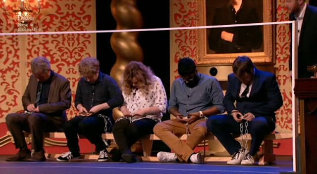 The cast of Taskmaster UK series 1 shackled to a bench on stage. They are looking at padlocks held in their hands. The cast of Taskmaster UK series 1 shackled to a bench on stage. They are looking at padlocks held in their hands.