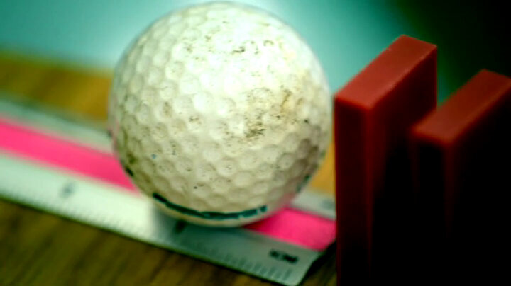 Golf Ball resting on a ruler next to two dominoes standing on end. Golf Ball resting on a ruler next to two dominoes standing on end.
