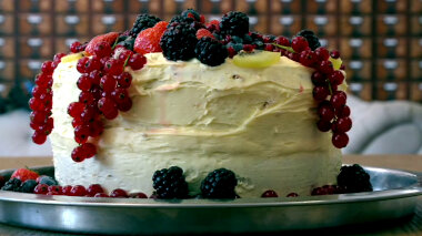 A layer cake with white frosting topped with fresh berries and sliced fruit.