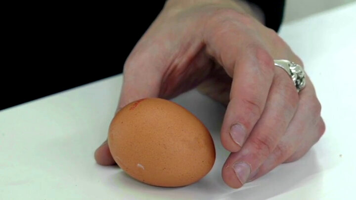 A hand reaching out to grasp an egg on a white table. A hand reaching out to grasp an egg on a white table.