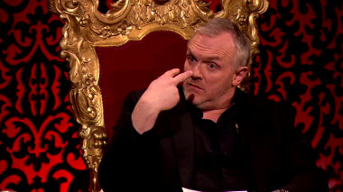 Greg Davies in his throne with eyebrows raised pointing two fingers of one hand at his eyes.
