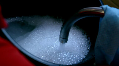 A faucet running water into a bucket full of soapy water.