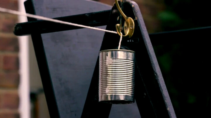 One end of a tin-can phone hanging from a hook attached to a lifeguard's chair. The string attached to the can continues out of frame. One end of a tin-can phone hanging from a hook attached to a lifeguard's chair. The string attached to the can continues out of frame.