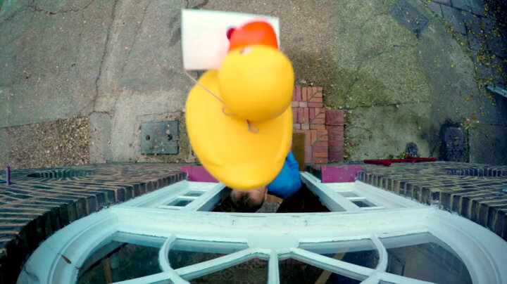 Aerial view of a large yellow rubber duck with a sealed task tied around its neck high above the Taskmaster house porch. Aerial view of a large yellow rubber duck with a sealed task tied around its neck high above the Taskmaster house porch.