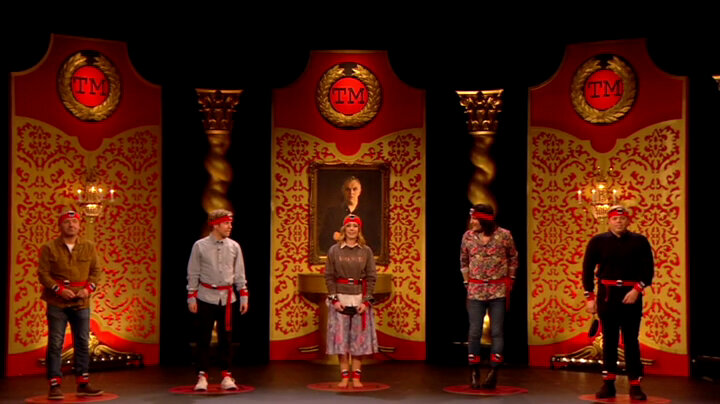 The cast of Taskmaster UK Champion of Champions 1 stand on the studio stage. Each contestant is wearing several pedometers attached to them with a red headband, red belt, red wrist-bands and red ankle-bands. The cast of Taskmaster UK Champion of Champions 1 stand on the studio stage. Each contestant is wearing several pedometers attached to them with a red headband, red belt, red wrist-bands and red ankle-bands.