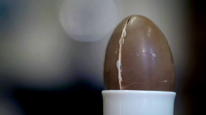 A chocolate egg with a visible seam halfway through rests in an eggcup. A chocolate egg with a visible seam halfway through rests in an eggcup.
