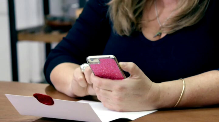 Liza Tarbuck holds a phone in a pink sparkly case over an open task brief on the living room table. Liza Tarbuck holds a phone in a pink sparkly case over an open task brief on the living room table.