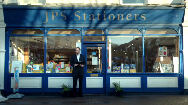 Alex Horne stands outside a blue and white shop building with JPS Stationers written on the shop's awning. Alex Horne stands outside a blue and white shop building with JPS Stationers written on the shop's awning.