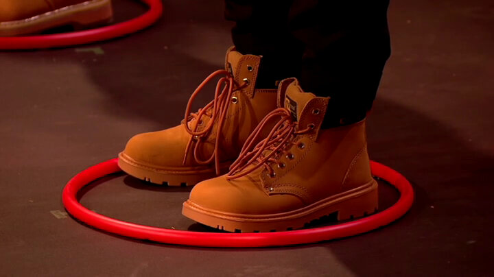A person in black trousers and tan work boots standing in a small red plastic hula-hoop. A person in black trousers and tan work boots standing in a small red plastic hula-hoop.