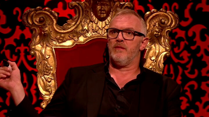 Greg Davies is sitting on his Taskmaster throne. He is gesturing with a black marker pen. Greg Davies is sitting on his Taskmaster throne. He is gesturing with a black marker pen.