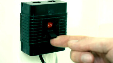 A hand about to switch a black plastic electrical switch from the on to the off position.