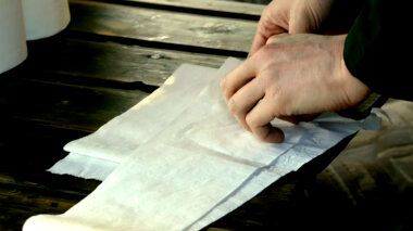 A pair of hands starting to fold a number of sheets of toilet paper.