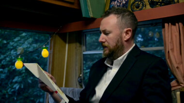 Alex Horne in the caravan reading a task.