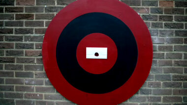 A close-up of a dark brick wall. On the wall is a red and black target. In the centre of the target is a sealed task.