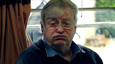 Close-up of an unhappy looking middle aged man sitting in the caravan.