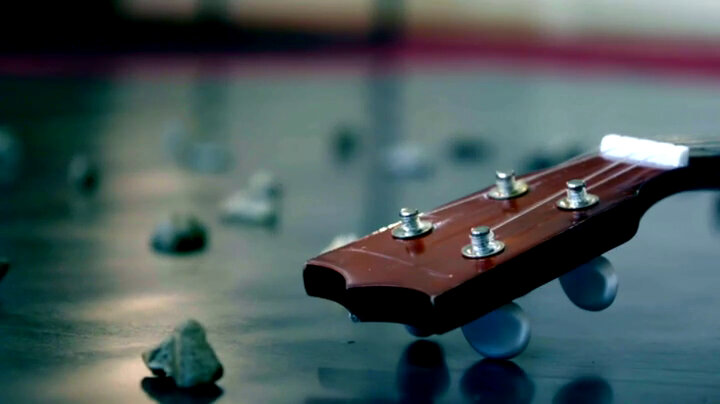 The head and neck of a ukulele on a black surface surrounded by many pebbles. The head and neck of a ukulele on a black surface surrounded by many pebbles.