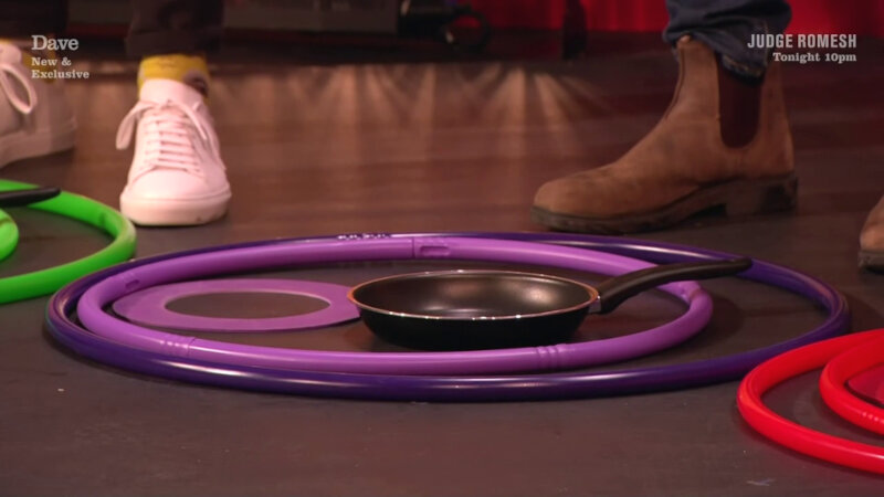 Three purple hoops and a frying pan on the Taskmaster studio stage. Parts of red and green hoops can also be seen. Joe Thomas' and Iain Stirling's feet can be seen behind the hoops. Three purple hoops and a frying pan on the Taskmaster studio stage. Parts of red and green hoops can also be seen. Joe Thomas' and Iain Stirling's feet can be seen behind the hoops.