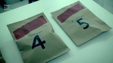 Two brown paper packages on a white table. Both have a red label that says 'Taskmaster Crisps'. One also says 'Flavour 4' and the other 'Flavour 5'.