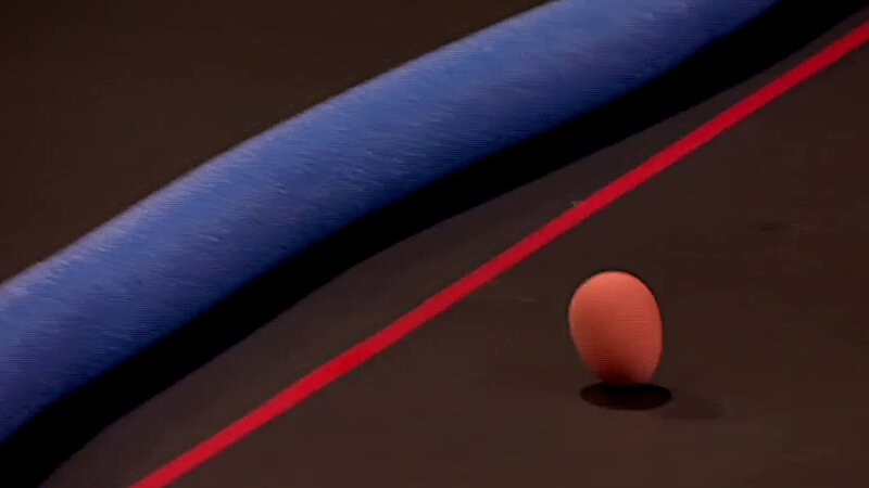 A close-up of the Taskmaster studio stage. On the stage is a rubber egg mid bounce. Behind the egg is a red tape line and a blue pool noodle. A close-up of the Taskmaster studio stage. On the stage is a rubber egg mid bounce. Behind the egg is a red tape line and a blue pool noodle.