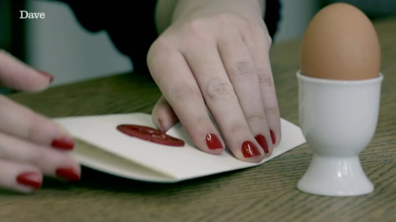A close-up of Katy Wix's hands opening a sealed task on top of a wooden table. Next to the task is a brown egg in a white egg cup. A close-up of Katy Wix's hands opening a sealed task on top of a wooden table. Next to the task is a brown egg in a white egg cup.