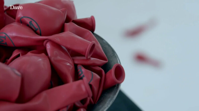 A pile of deflated red balloons with the Taskmaster logo in black resting in a grey bowl.