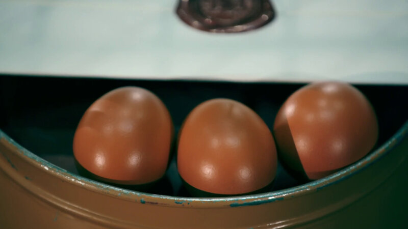 Three brown chicken eggs and a sealed task resting on the bottom of an overturned brown metal bucket.