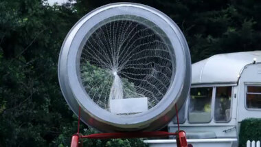 A metal bagging machine with mesh bags. The Taskmaster caravan can bee seen behind it. Resting on the bagging machine is a sealed task.