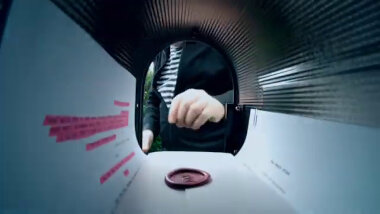 Camera POV shot from inside the mail box next to the caravan. Inside the mailbox is a sealed task lying on top of a script. The script can not be read.