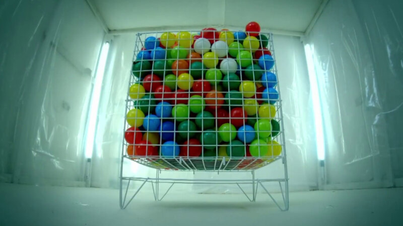 A square wire basket in the Taskmaster house lab. The basket is filled with many brightly coloured balls.