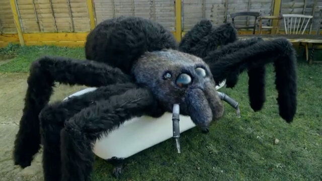 A giant stuffed spider sitting on a white ottoman in the Taskmaster house garden.