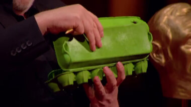 Greg Davies holding a green egg carton while on his Taskmaster studio throne.