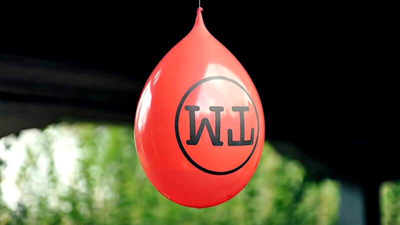 A balloon filled with water hangs upside-down under an arch.