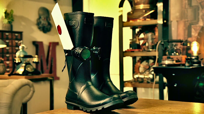 Two wellies stand on the living room table. One wellie has a pair of dark goggles with a camera attached wrapped around it. A sealed task brief is stuck in the elastic band of the goggles. Two wellies stand on the living room table. One wellie has a pair of dark goggles with a camera attached wrapped around it. A sealed task brief is stuck in the elastic band of the goggles.
