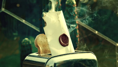A toaster. In one side of the toaster is a piece of toast. In the other side of the toaster is a scorched and smoking sealed task brief.