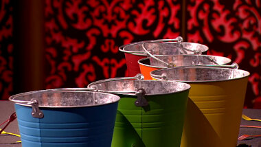 Five colourful metal buckets on the studio stage. Coloured cutlery is strewn around the buckets.