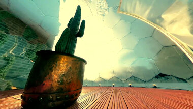 A cactus in a large metal pot in the plastic dome.