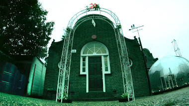 A metal wedding bower stands in the driveway. A sealed task brief is hanging from the centre of the bower.