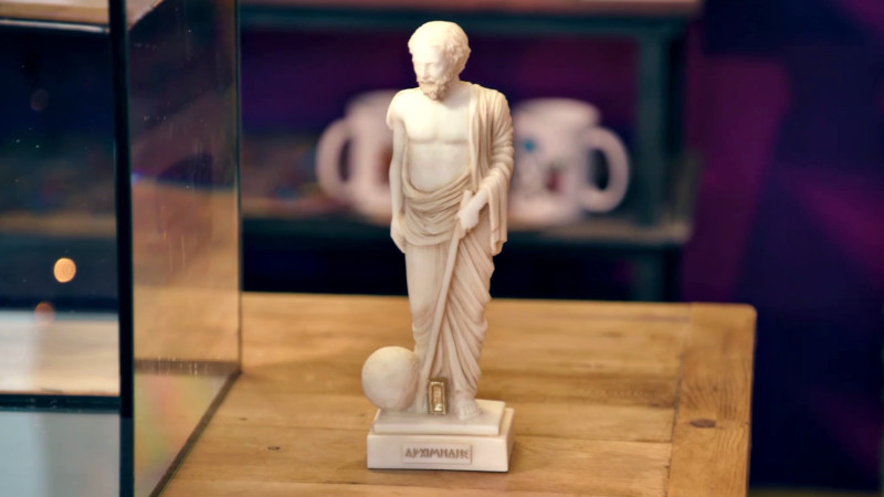 A statuette of Archimedes on a wooden table next to a fish tank partially filled with water. A statuette of Archimedes on a wooden table next to a fish tank partially filled with water.