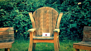 A wooden chair in the garden in between two wooden benches. There's a sealed task brief on the chair.