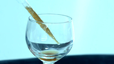 A pipette filled with an amber-coloured liquid drips into a wine glass.