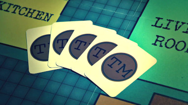 Five playing cards with the TM logo display on a Cluedo-styled Taskmaster house game board.