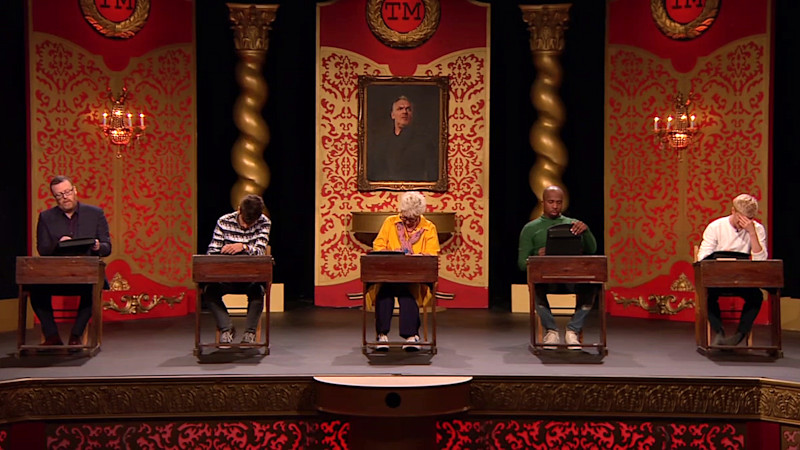 The cast of series 15 seated at school desks on the Taskmaster studio stage. The cast of series 15 seated at school desks on the Taskmaster studio stage.