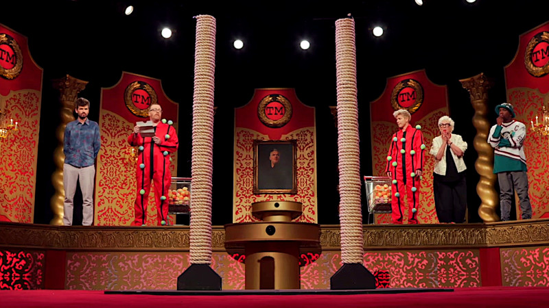 The cast of UK series 16 on the studio stage. Mae and Frankie are wearing red boiler suits with Velcro stripes and many fabric balls attached to those stripes. The rest of the cast are dressed normally. A shopping cart full of more balls is at either side of the stage. On the lower floor are two large scratching posts. Frankie reads out the task. The cast of UK series 16 on the studio stage. Mae and Frankie are wearing red boiler suits with Velcro stripes and many fabric balls attached to those stripes. The rest of the cast are dressed normally. A shopping cart full of more balls is at either side of the stage. On the lower floor are two large scratching posts. Frankie reads out the task.