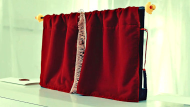 A small set of red theatre curtains in a frame on the lab table with a yellow rubber duck on each corner of the frame. A sealed task brief rests next to the curtains.