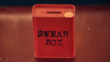 A metal bank labelled 'Swear Box' with a coin resting on top.